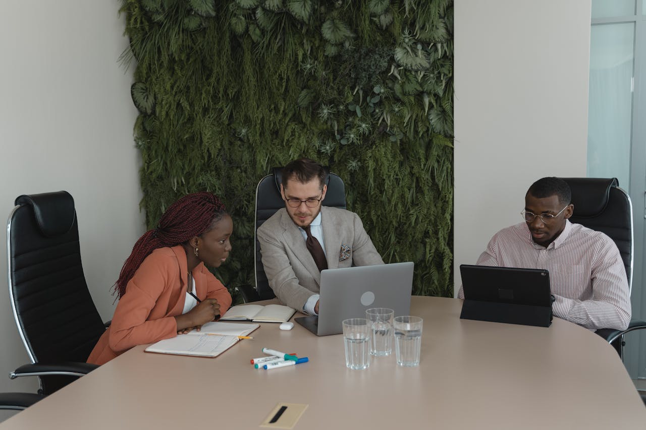 Business professionals engaged in a team meeting with laptops in a modern office setting with green wall decor.